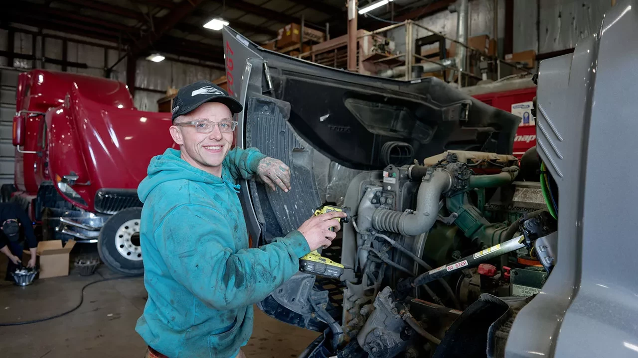 BST technician repairing semi-truck engine inside maintenance shop