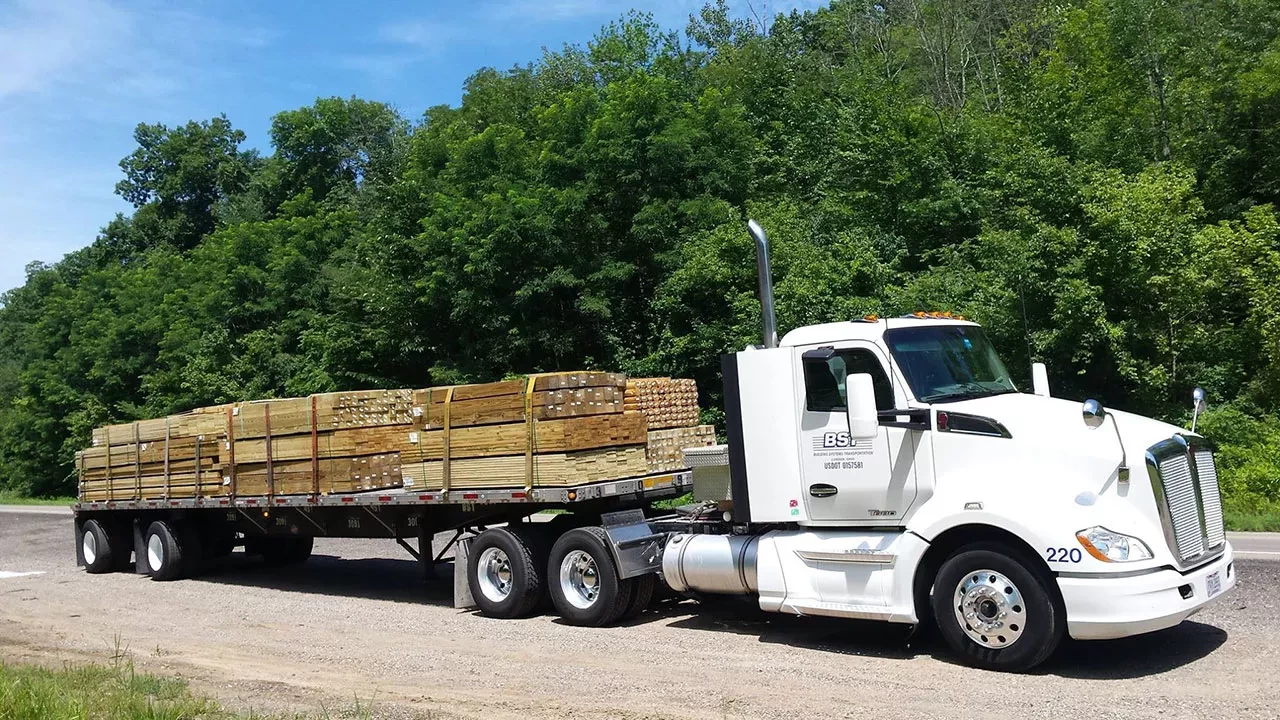 BST flatbed semi-truck hauling lumber on highway near wooded area Image