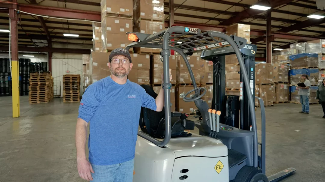BST warehouse employee standing beside forklift inside storage facility